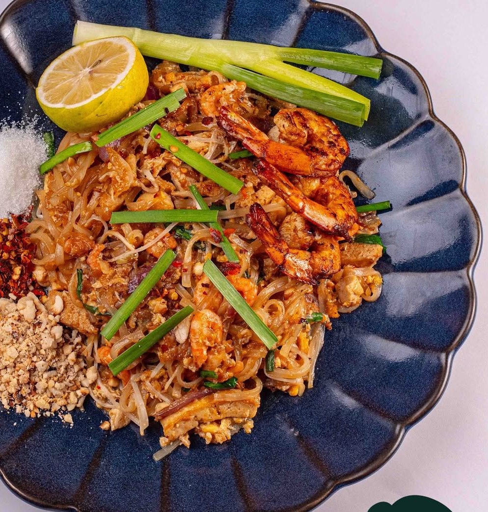 Shrimp Pad Thai on a dark scalloped plate with lime and peanuts